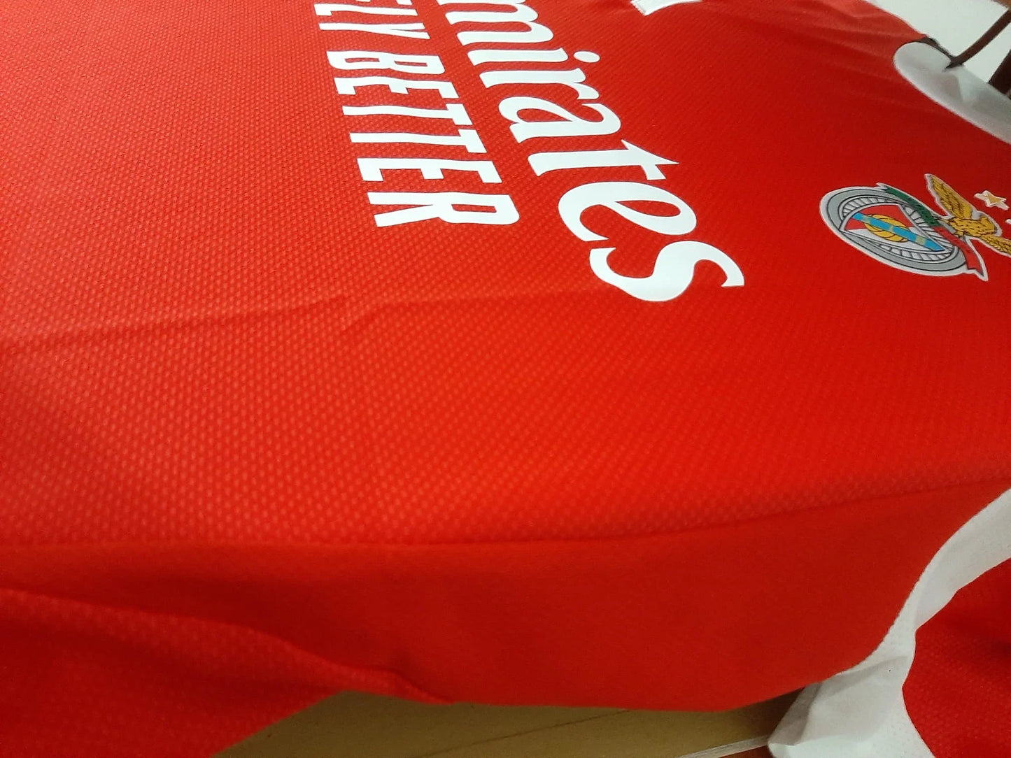 Close-up lateral da camisola principal do Benfica 25/26 mostrando a textura do tecido slim fit e patrocinadores.