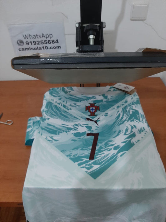 Camisola alternativa de Portugal 2026 branca e verde-mar com o número 7 estampado na frente, posicionada numa prensa térmica de personalização