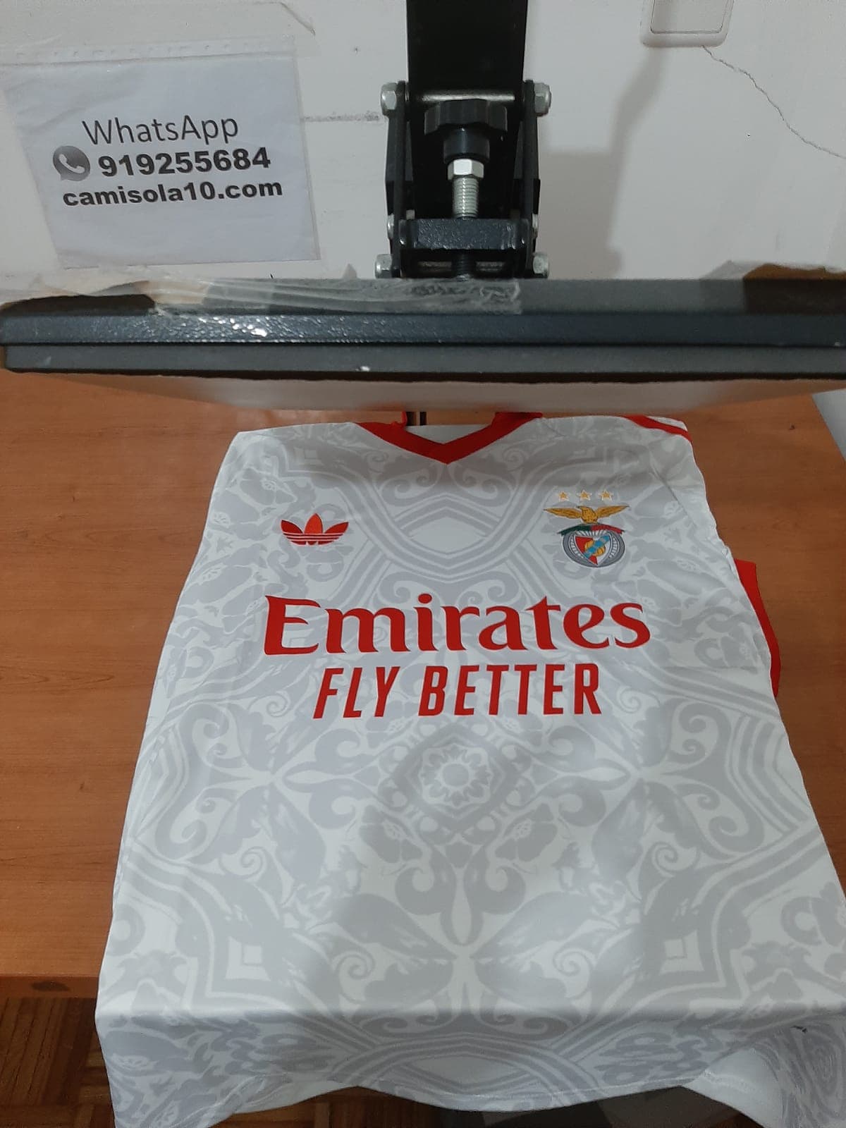 Frente da camisola alternativa branca do SL Benfica 26/27 , emblema do clube e patrocinador Emirates.