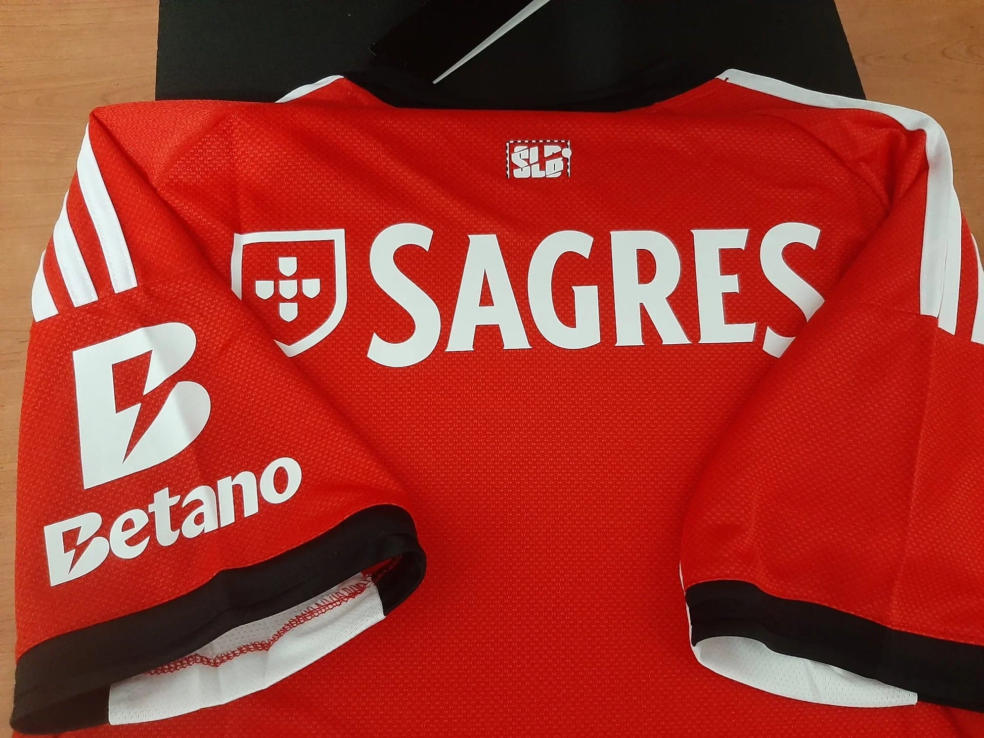 Pormenor das costas e manga da camisola do Benfica 25/26 exibindo os patrocínios Sagres e Betano.