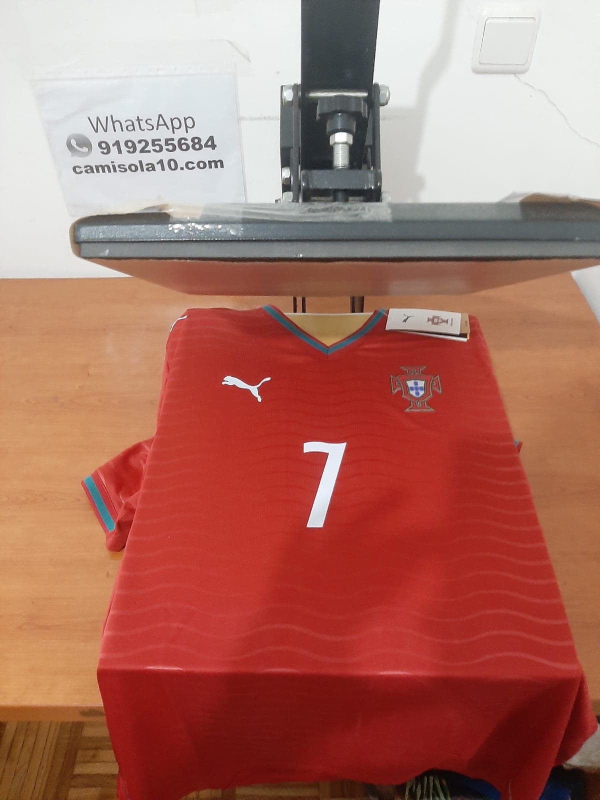 Camisola principal de Portugal 2026 vermelha com o número 7 estampado na frente, posicionada numa prensa de personalização profissional
