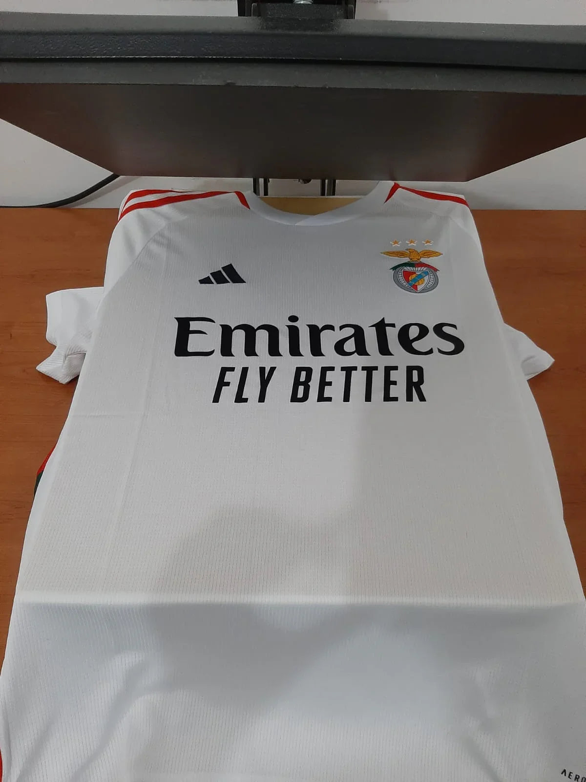 Vista frontal da terceira camisola branca do SL Benfica época 23/24 na prensa de personalização.