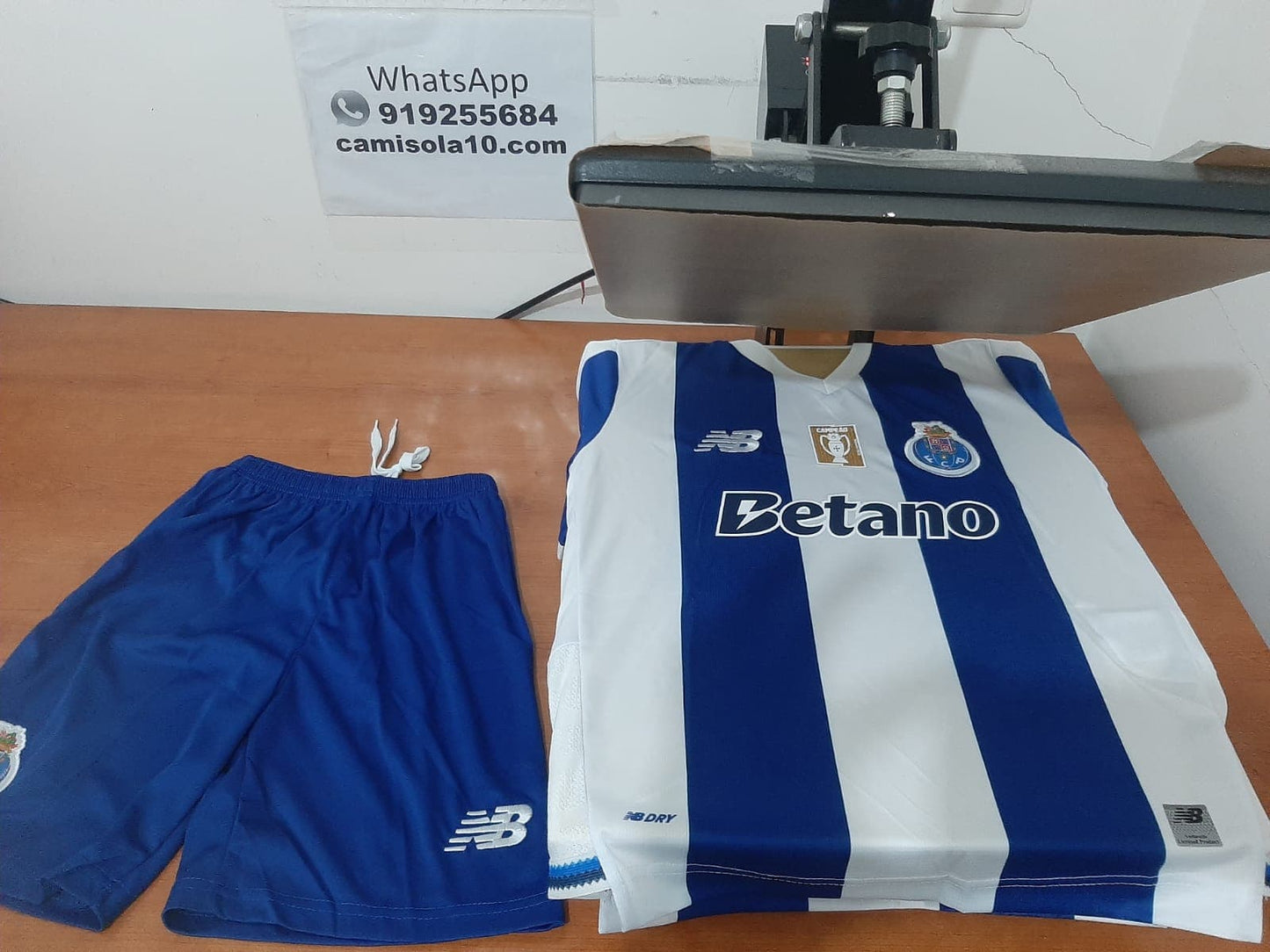 Frente do kit infantil do FC Porto 26/27 destacando o emblema do clube, patrocinadores New Balance e Betano e os calções azuis | Badge de campeão