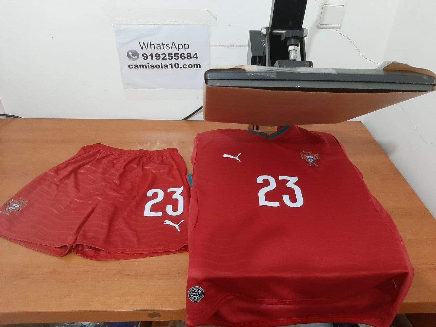 Frente do kit de criança principal de Portugal 2026 com o número 23 estampado nos calções e na camisola vermelha.